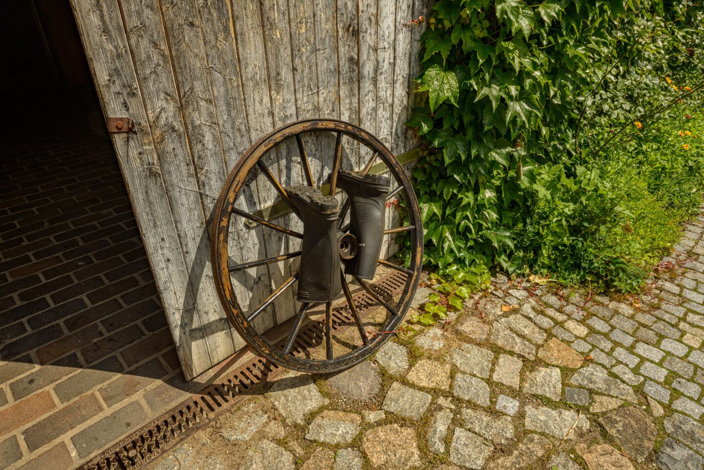 Stiefel zum trocknen an einem alten Speichenrad aufgehängt und am Scheunentor lehnend
